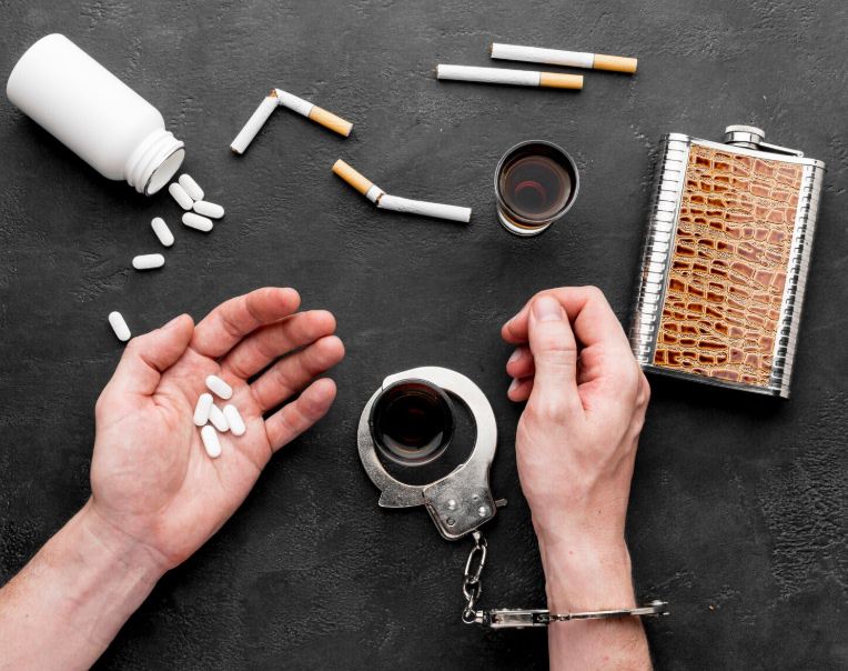 Manos sosteniendo pastillas junto a cigarrillos y alcohol